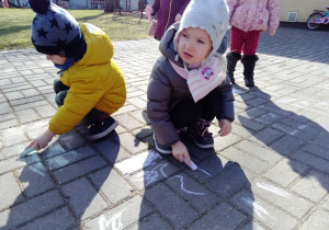 Chłopiec i dziewczynka malują kolorowymi kredami płyty chodnika